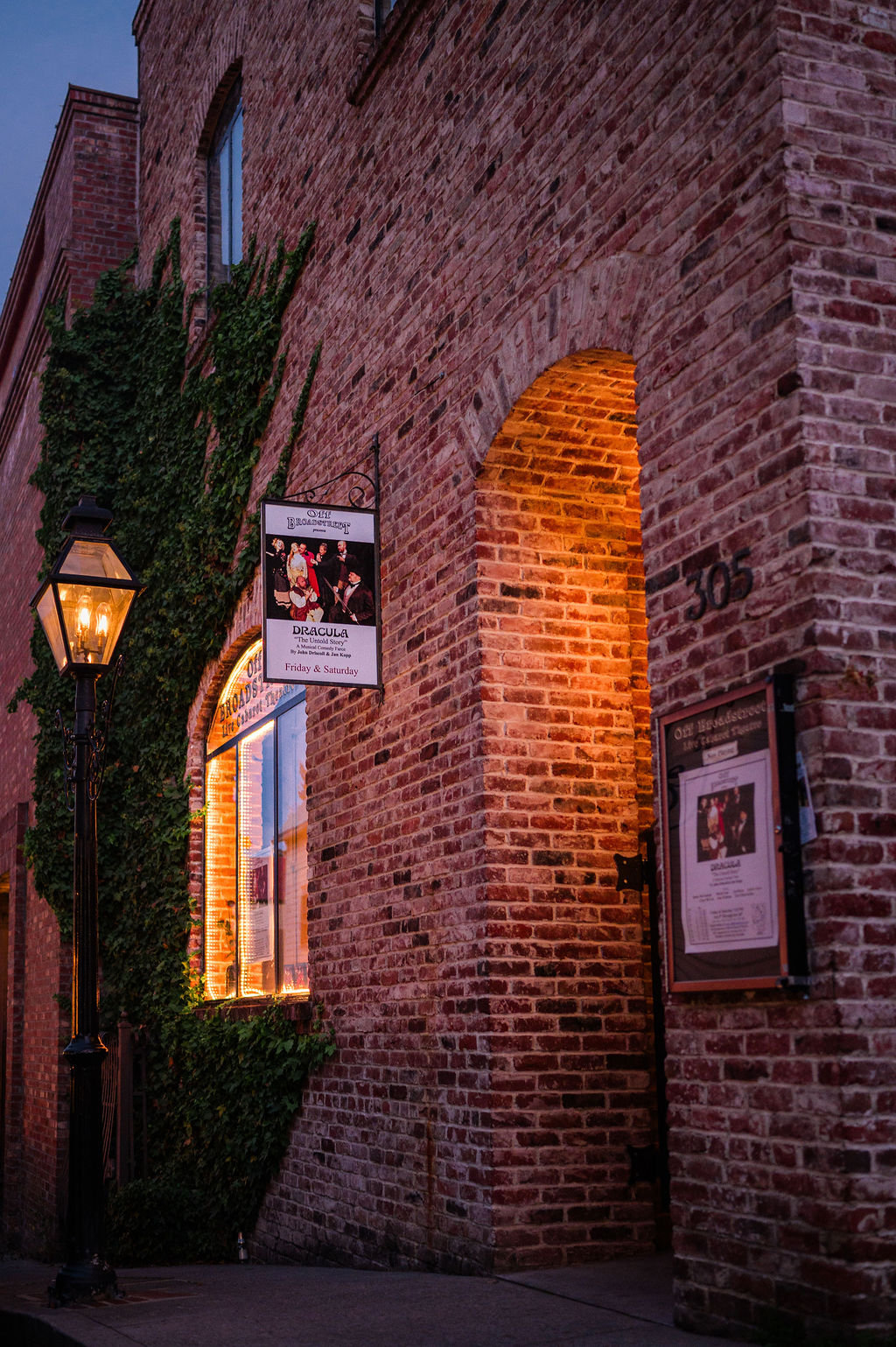 The lit brick entrance of Off Broadstreet theatre at dusk, with a playbill sign under a gas lamp